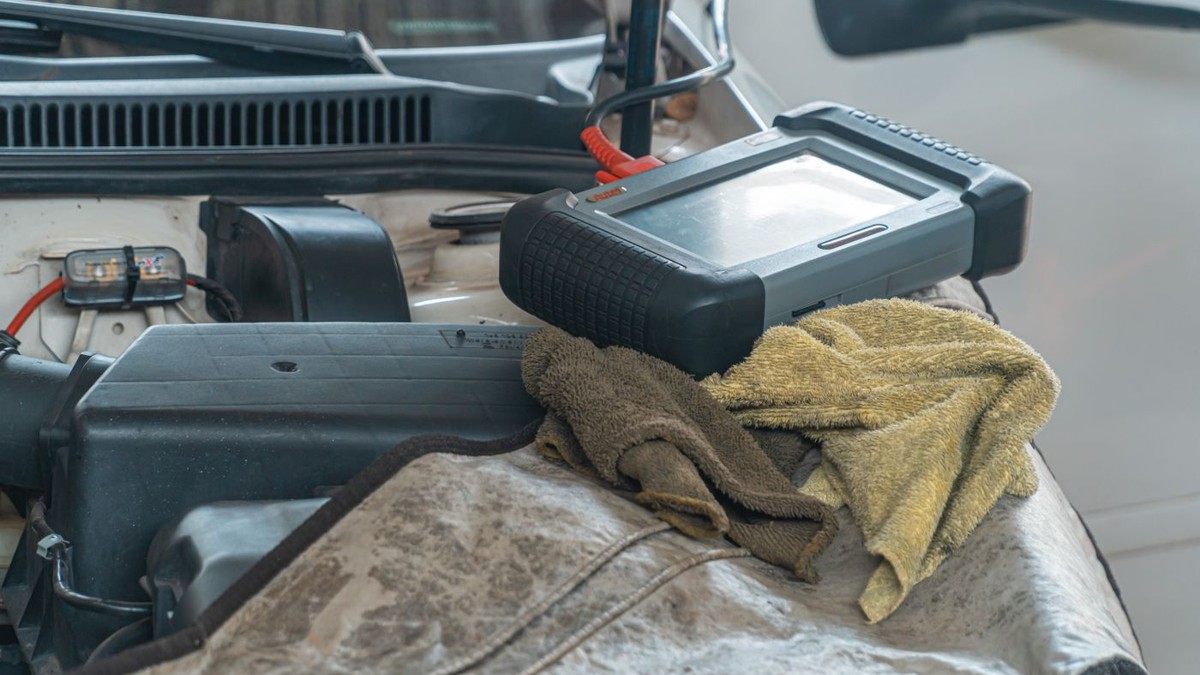 Stock photo: diagnostic scanner resting on a protective cloth in an open engine bay, with a red cable attached.