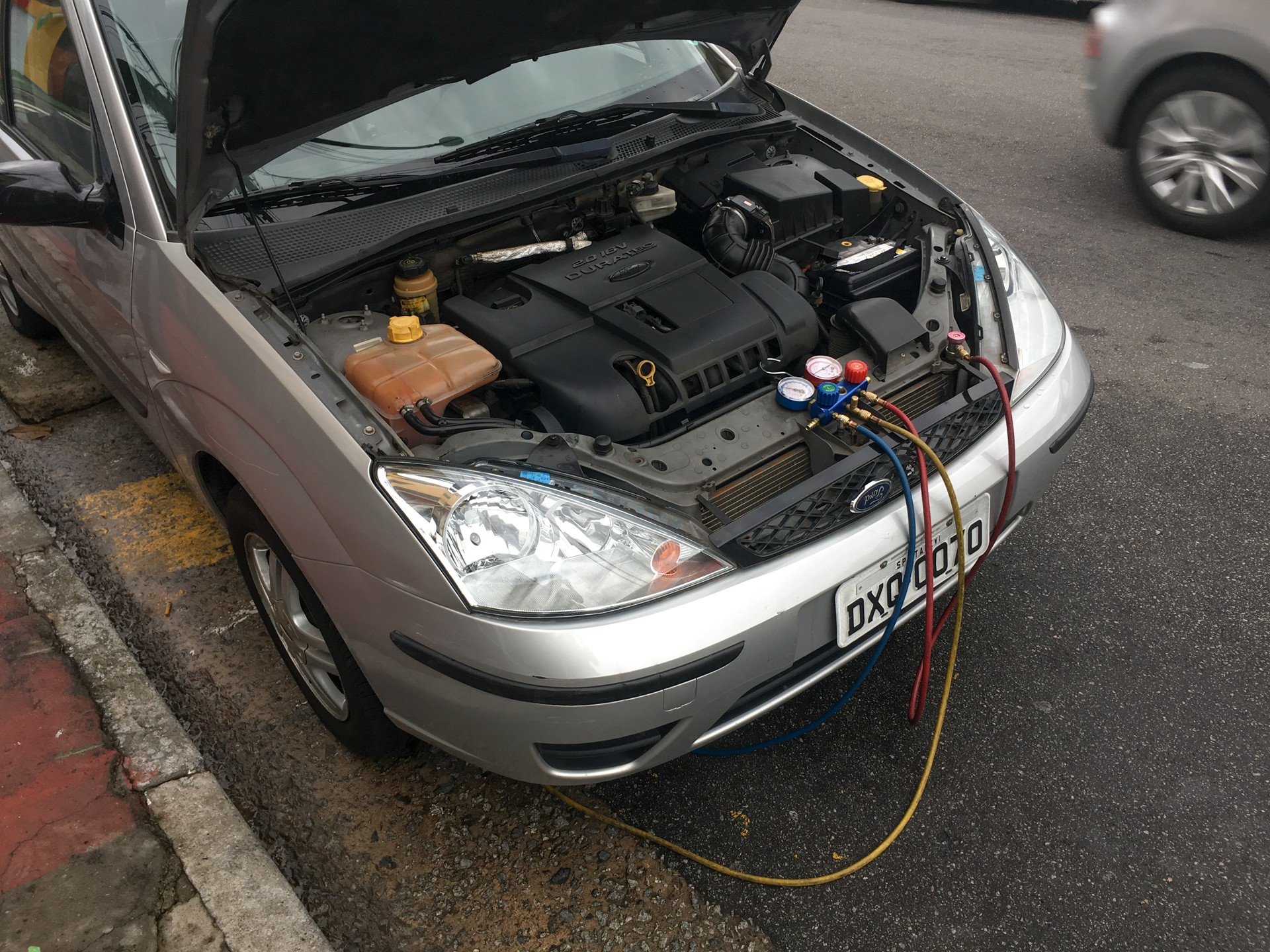 Stock photo: refrigerant manifold gauges and service hoses connected to a Ford Focus with its hood open.