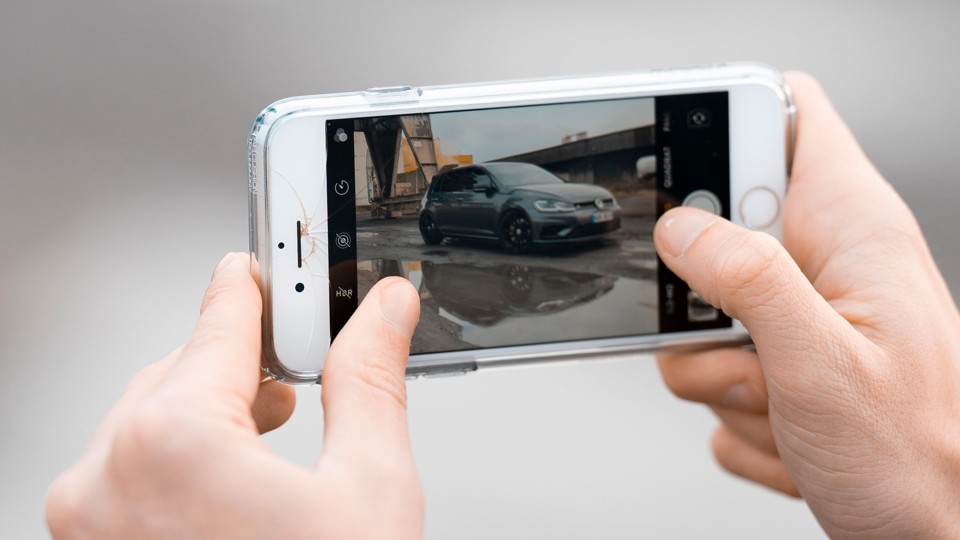 Stock photo: close-up of hands photographing a car exterior with a smartphone camera.