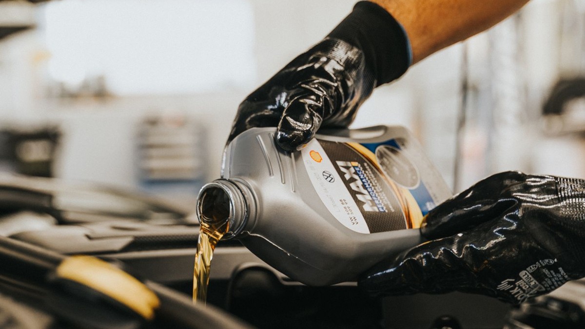 Stock photo: gloved mechanic pouring fresh engine oil from a bottle into a car engine.
