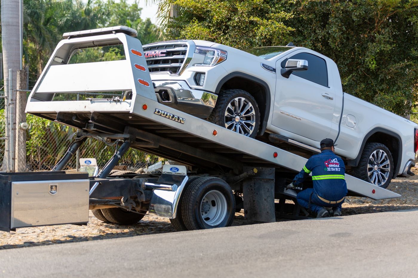 Stock photo: operator beside a tilted flatbed tow truck carrying a white GMC pickup.