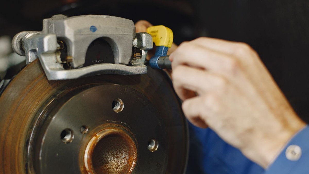 Stock photo: close-up of a mechanic using a tool on a brake caliper above an exposed disc rotor.
