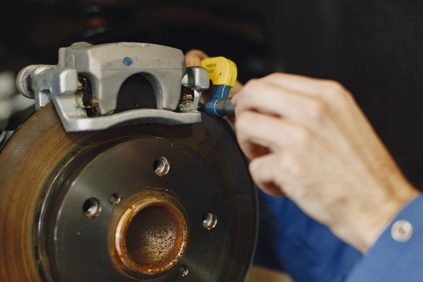 Stock photo: close-up of a mechanic using a tool on a brake caliper above an exposed disc rotor.