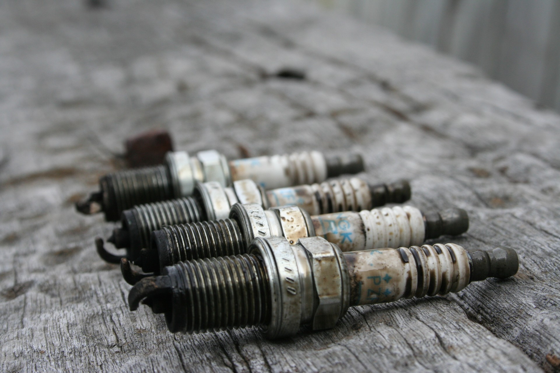 Stock photo: four used spark plugs laid out for inspection, with visible electrodes and ceramic insulators.