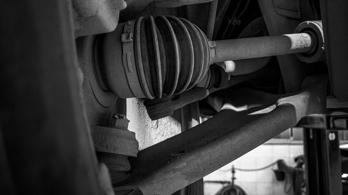 Stock photo: black-and-white close-up of an installed CV axle and ribbed joint boot beside a wheel and suspension components.