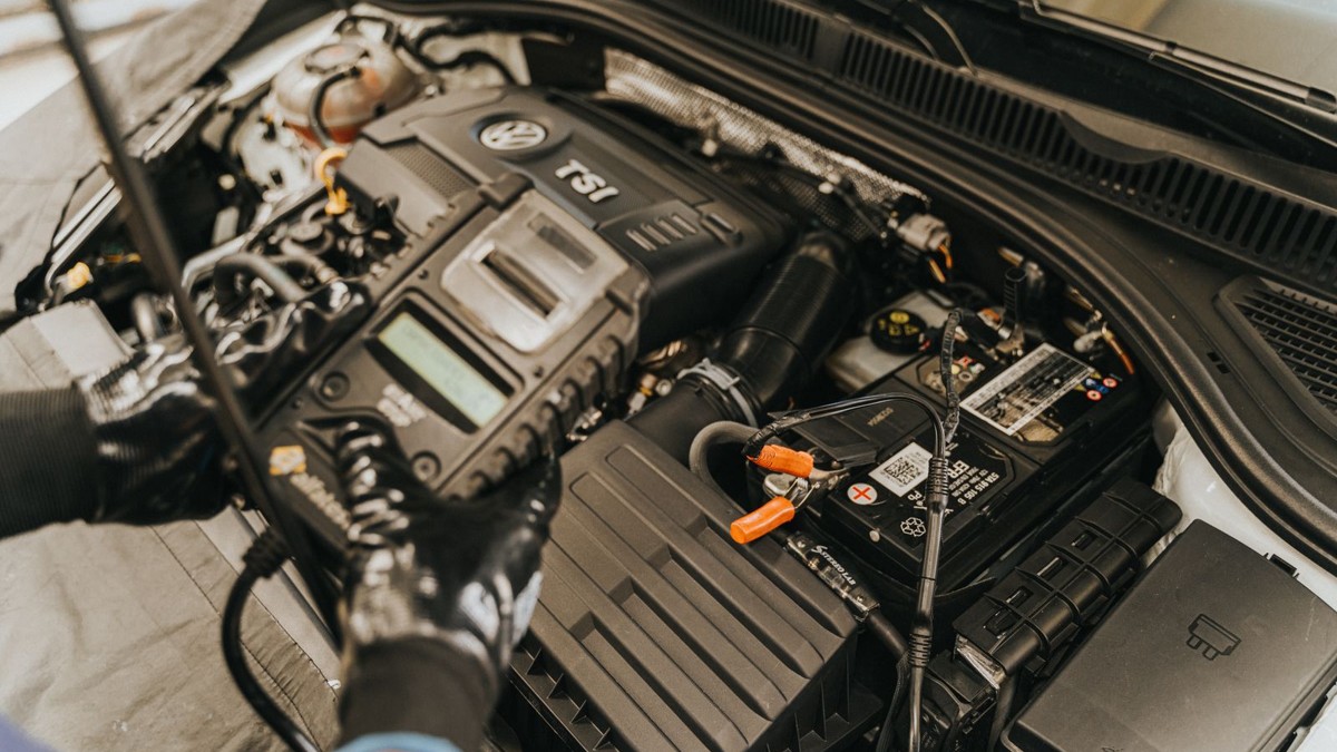 Stock photo: gloved technician holding a battery tester over a car battery in an engine compartment.