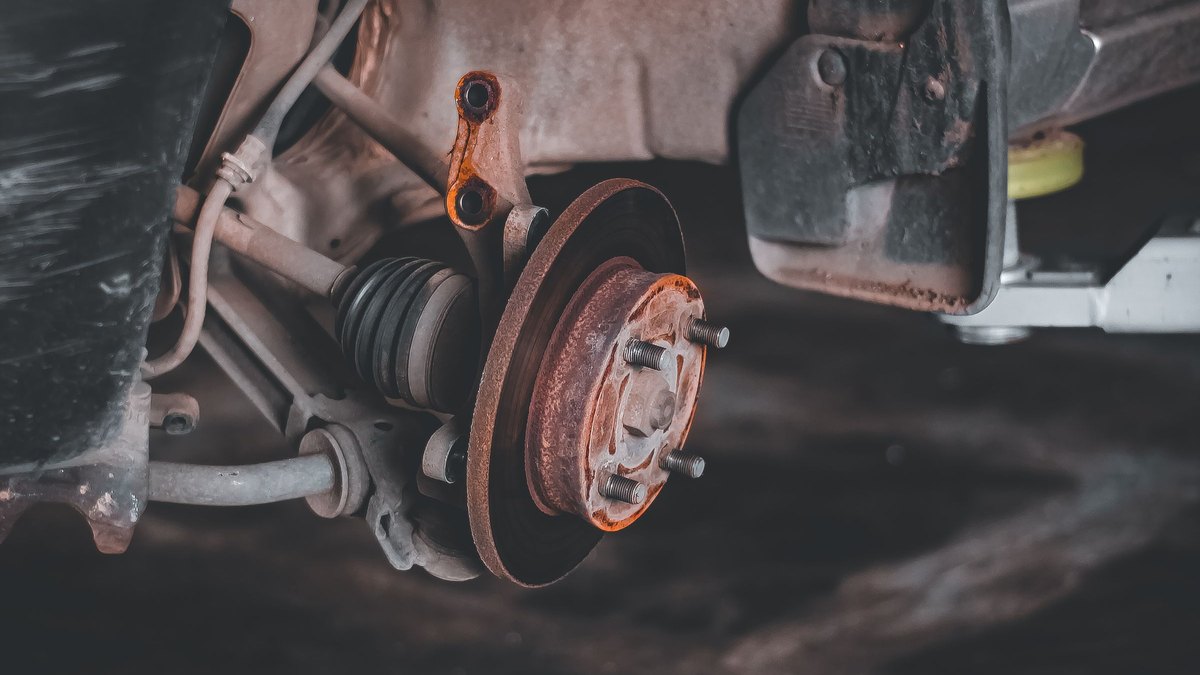 Stock photo: rusted wheel well with the wheel removed, showing the strut mount, control arms, CV joint boot, brake rotor, and rusty wheel hub.